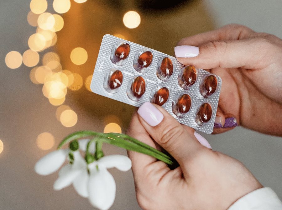 A hand holding a blister pack of medication next to a small flower
